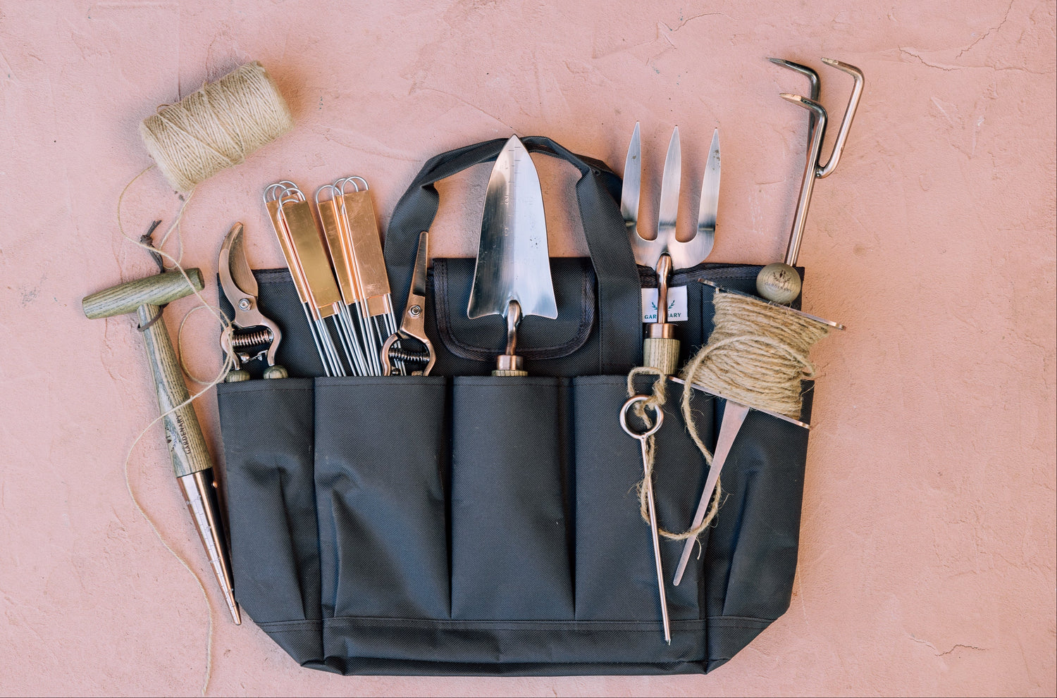 Gardening tools in a black tool belt on a pink surface