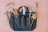 Gardening tools in a black tool belt on a pink surface