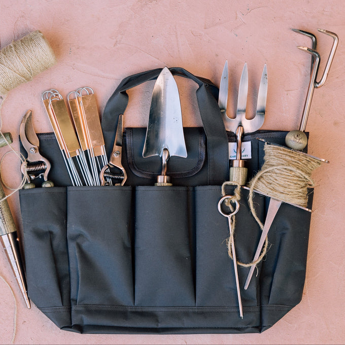 Gardening tools in a black tool belt on a pink surface