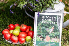 Tomatoes on a plate with a plant and 'Kitchen Garden Revival' book on grass